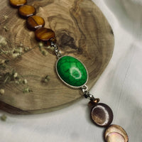 Close-up of handmade bracelet with green turquoise stone and brown beads on metal links.