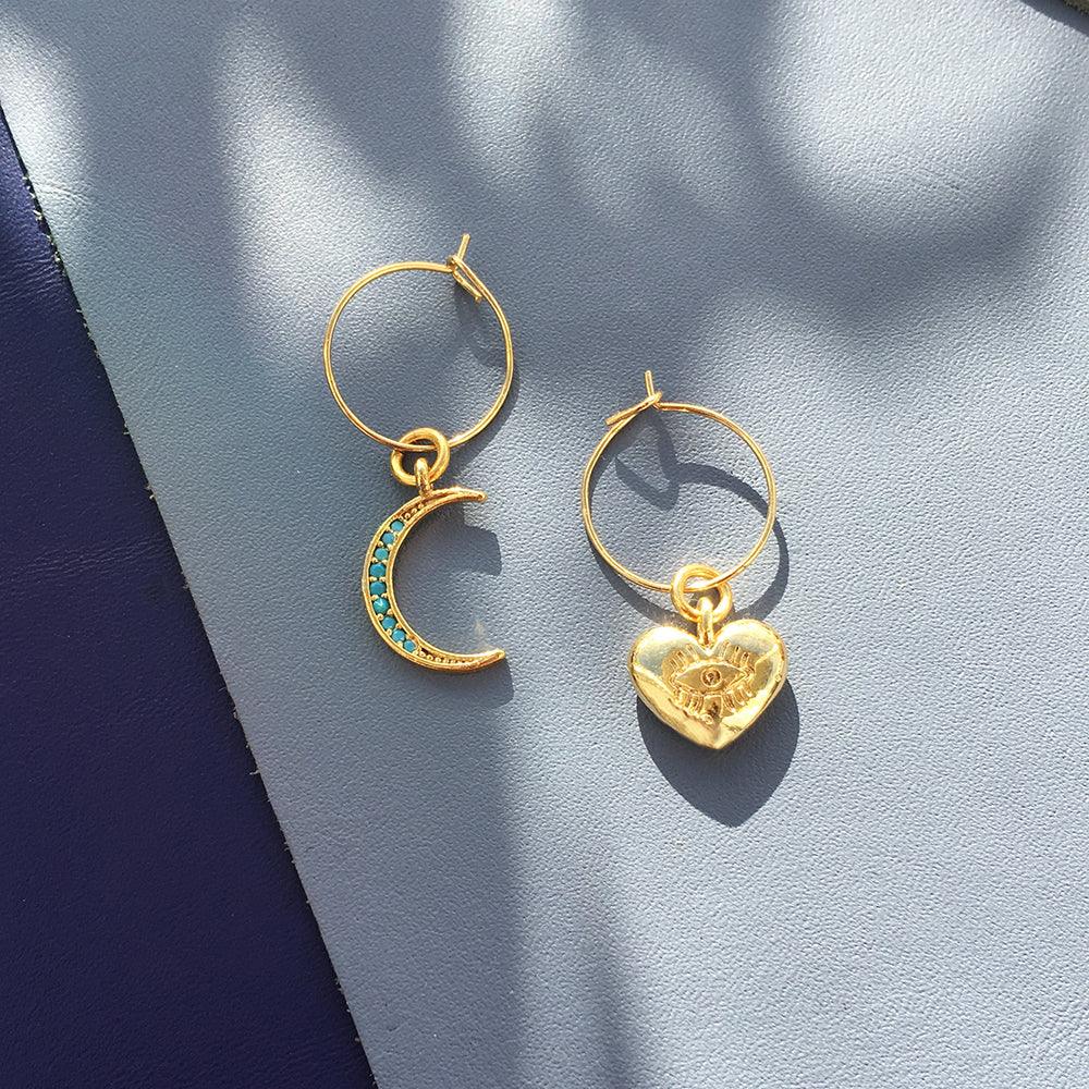 Turquoise moon and gold heart charm earrings displayed on pale pink dish with gold accents.