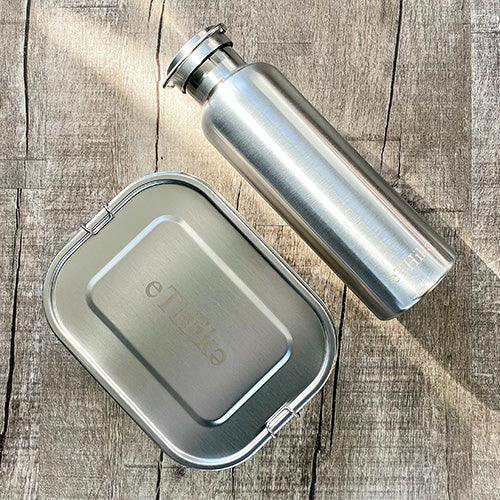 Zero waste starter kit with stainless steel bento-style lunchbox and water bottle on a wooden table.