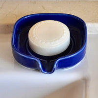 Close-up of glossy white ceramic soap dish showing water droplets draining away.