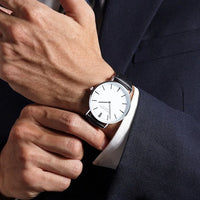 Men's watch with brown leather strap placed on a wooden table with sunlight highlighting its copper dial.