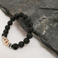 Black lava stone bracelet with silver skull bead and spacers laid out on white background