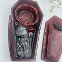Close-up of spooky coffin tealight holder decorated with purple amethyst and a resin skeleton hand detail.