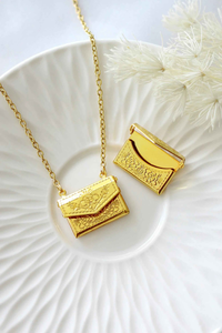 Gold-plated envelope locket necklace with delicate daisy engraving, displayed on a soft neutral background.