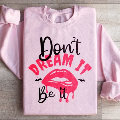 Close-up of peach-colored sweatshirt fabric with 'Don't Dream It' design in white text.