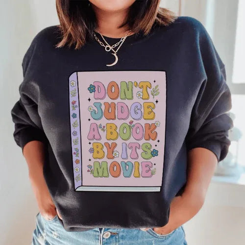 Black 'Don't Judge A Book' sweatshirt with peachy pink text, close-up showing fabric texture and fit.