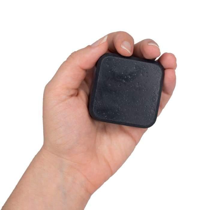Hand holding charcoal facial soap above wooden surface with wallet and device nearby