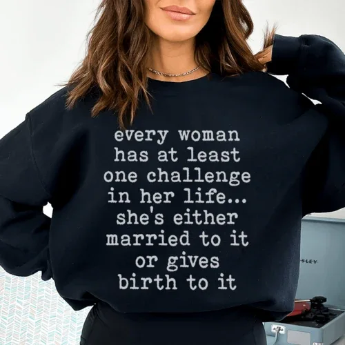Close-up of black sweatshirt fabric showing white text 'Every Woman Has At Least One Challenge In Life'.