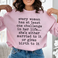 Light pink sweatshirt featuring the phrase 'Every Woman Has At Least One Challenge In Life' in white text.