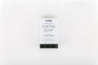 Activated charcoal coffee soap bar on a beige cloth with coffee beans and a rustic natural background.