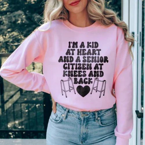 Light pink sweatshirt featuring 'I'm A Kid At Heart And A Senior Sitizen' text in white and peach colors.