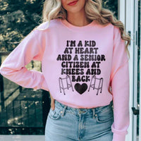 Light pink sweatshirt featuring 'I'm A Kid At Heart And A Senior Sitizen' text in white and peach colors.