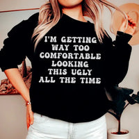 Black sweatshirt with white and pink text reading 'I'm Getting Way Too Comfortable Looking This Ugly All The Time'.