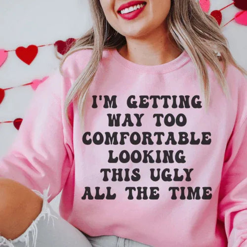 Light pink sweatshirt showing phrase 'I'm Getting Way Too Comfortable Looking This Ugly All The Time' in white and pink