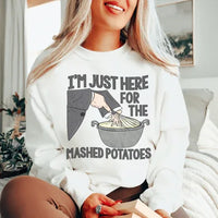 Folded peachy pink sweatshirt with 'I'm Just Here For The Mashed Potatoes' text visible on front.