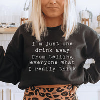 Peach-colored sweatshirt with text 'I'm Just One Drink Away' on front, cozy fleece fabric visible.