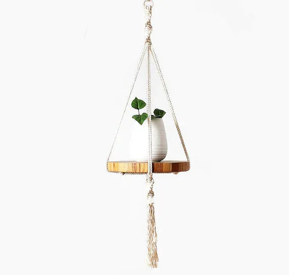 Handcrafted ecru cotton macrame plant hanger holding a potted plant with long tassels and wooden tray.