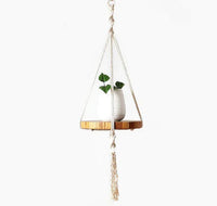Handcrafted ecru cotton macrame plant hanger holding a potted plant with long tassels and wooden tray.