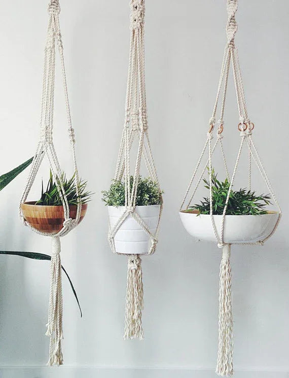 Hand-crafted macrame plant hanger in natural cotton rope holding a small potted plant against a white wall.