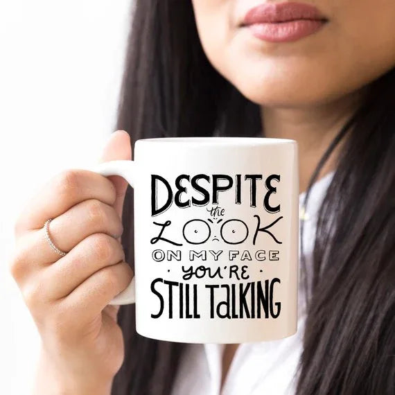 White coffee mug with black text Saying Despite The Look On My Face You're Still Talking