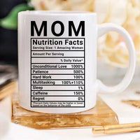 White coffee mug with 'Mom Nutrition Facts' label and humorous text, placed on a light wooden surface.