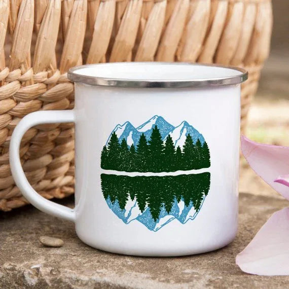 Enamel mug placed outdoors on rock, showing mountain design and stainless steel rim detail.