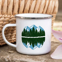 Enamel mug placed outdoors on rock, showing mountain design and stainless steel rim detail.