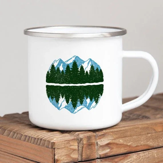 White enamel camping mug with blue mountain design and stainless steel rim, shown on wooden surface.