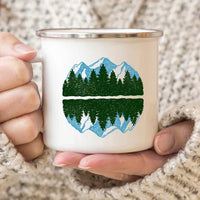 Enamel mug with scenic mountain print, set on wooden surface with natural light highlighting details.