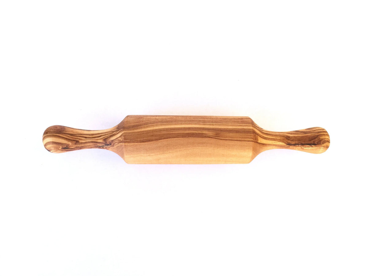 Mini rolling pin placed on a wooden cutting board alongside cookie dough and baking tools.