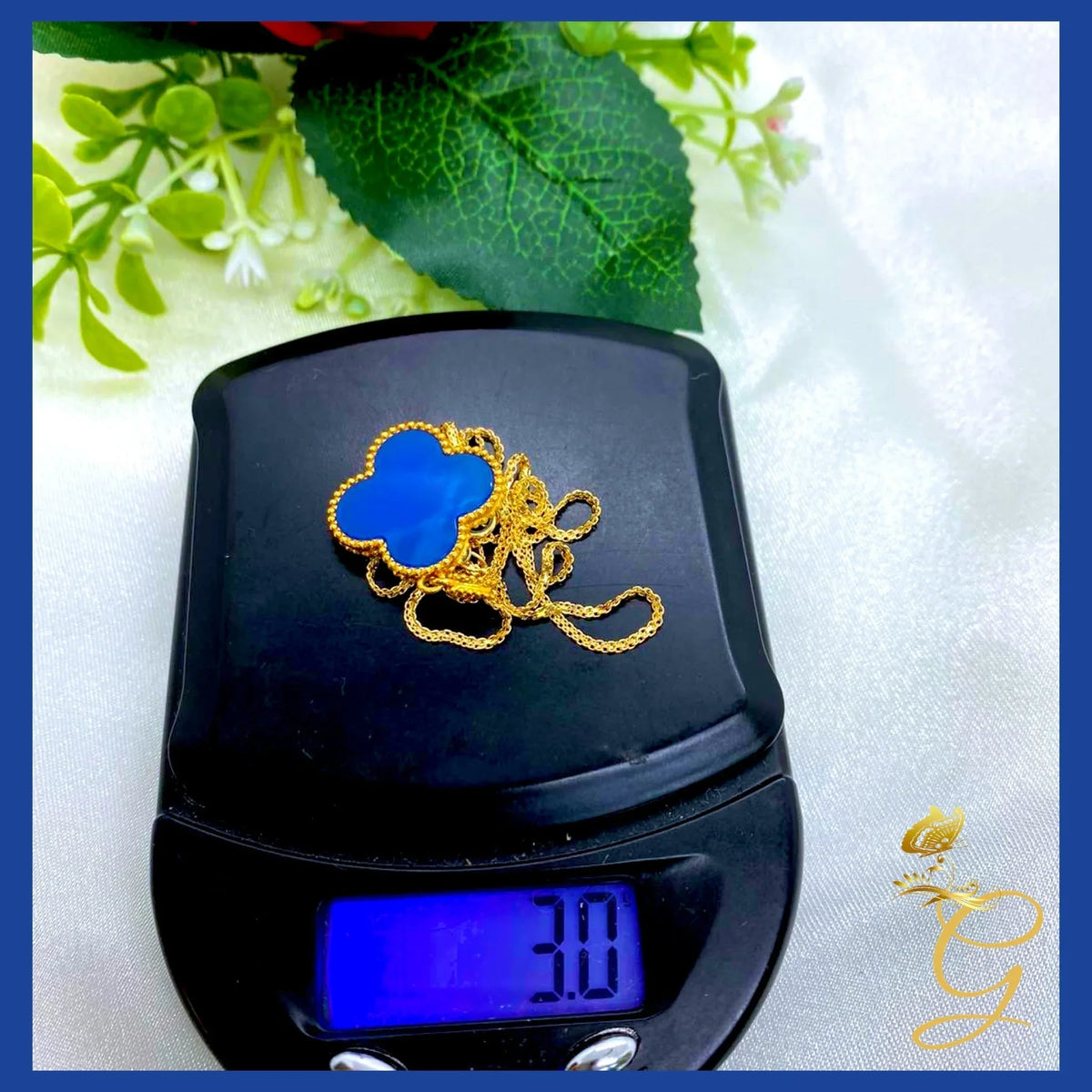 Blue cloverleaf shaped pendant necklace made of 18K yellow gold displayed on a soft white fabric.