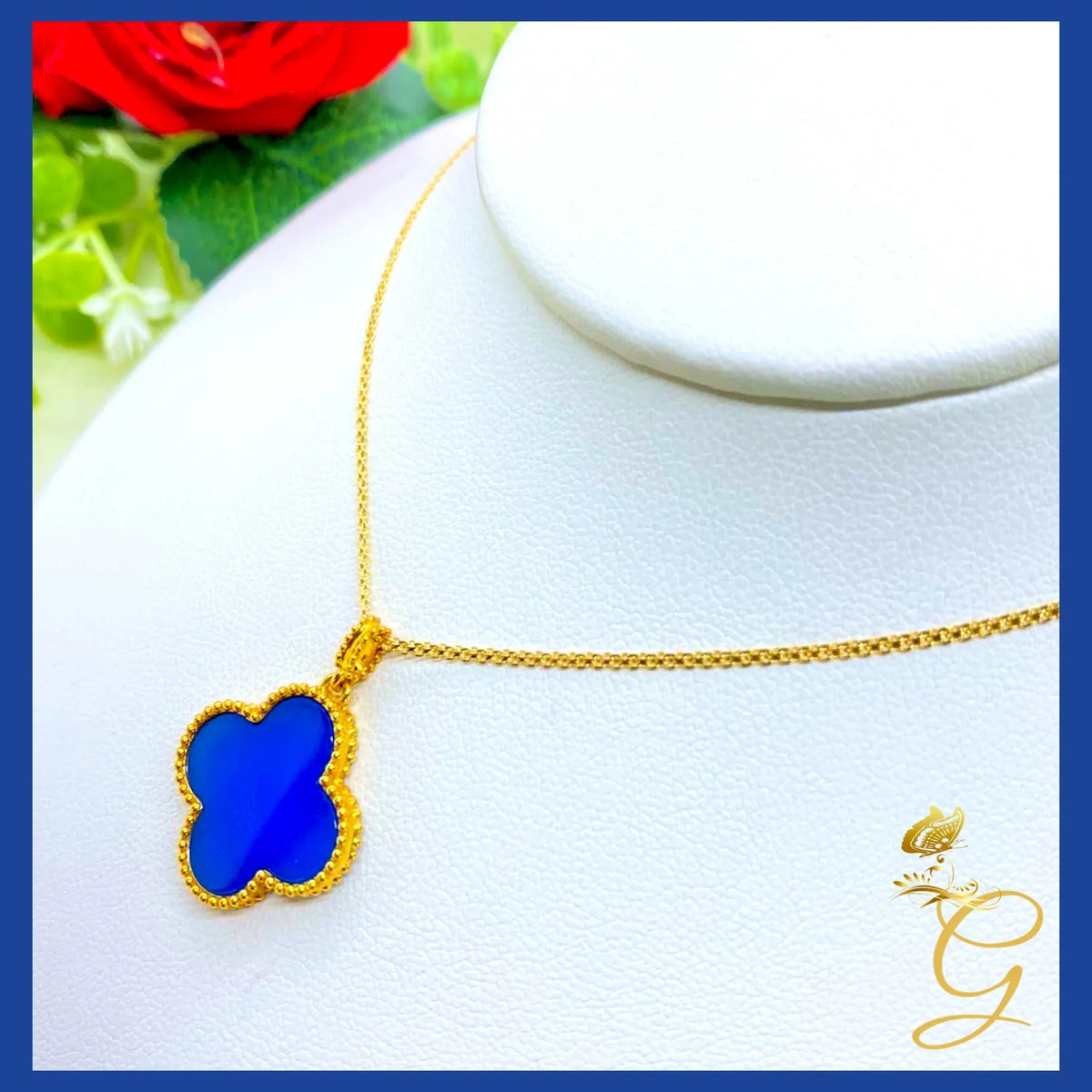 Close-up of 18K yellow gold cloverleaf pendant with blue accent on an 18-inch chain on white background.