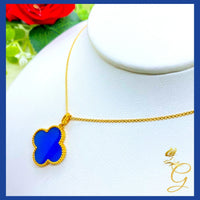 Close-up of 18K yellow gold cloverleaf pendant with blue accent on an 18-inch chain on white background.