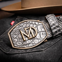 Individual adjusting gray caiman crocodile belt over blue denim pants.