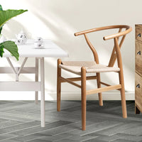 Lifestyle image of a dining area featuring two wooden chairs with rattan seats around a table.