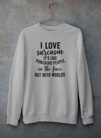 Light gray 'I Love Sarcasm' sweatshirt shown from front, hanging on hanger on concrete wall.