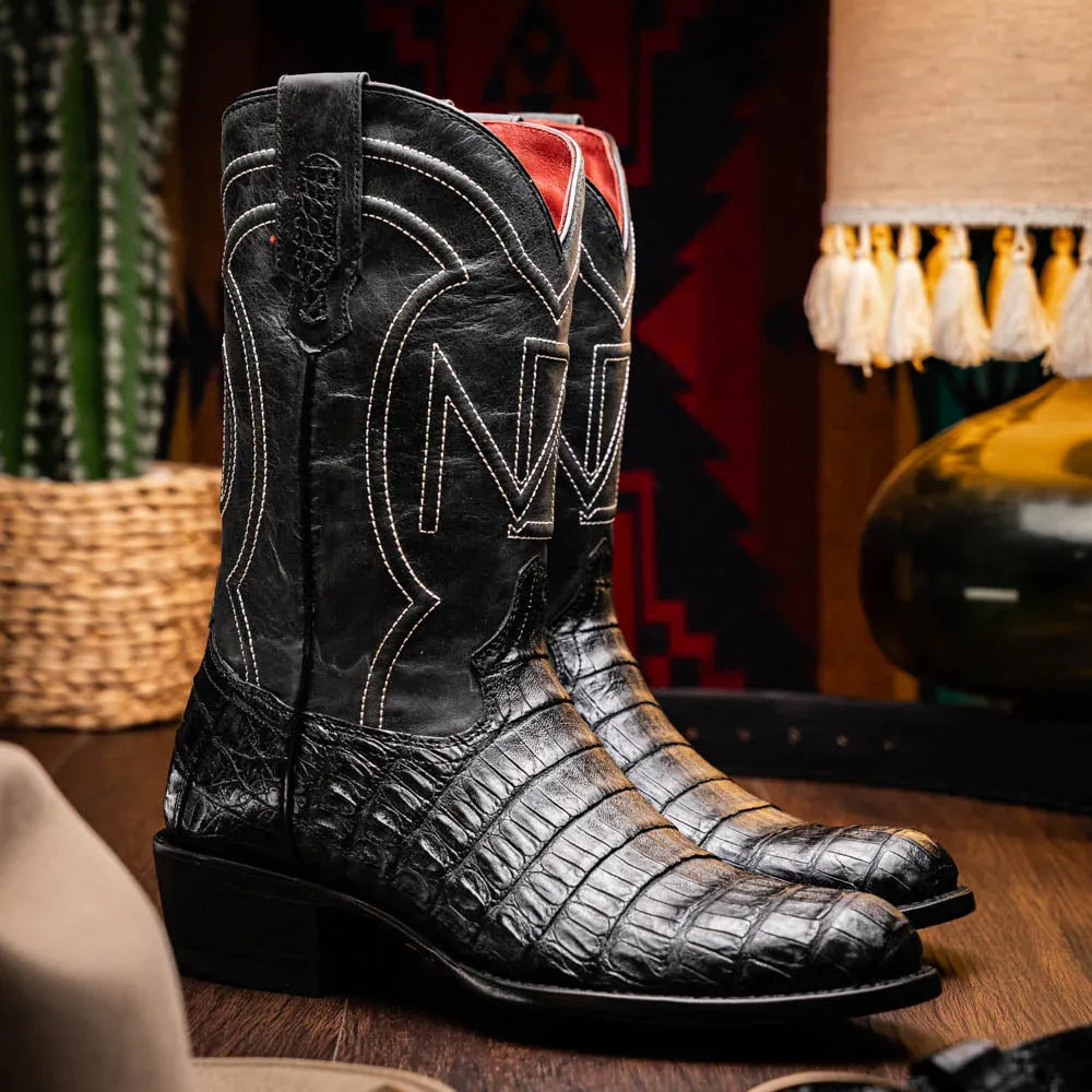 Man wearing black caiman skin cactus boots standing outdoors on wooden surface