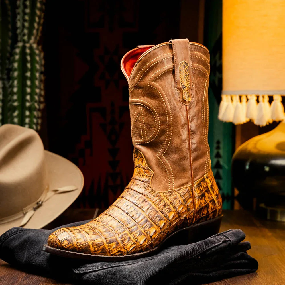 Side view of man walking in mustard brown caiman cowboy boots paired with rolled jeans outdoors.