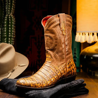 Side view of man walking in mustard brown caiman cowboy boots paired with rolled jeans outdoors.