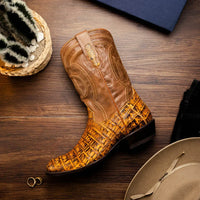 Man sitting on stairs wearing mustard brown caiman belly skin cowboy boots with jeans.