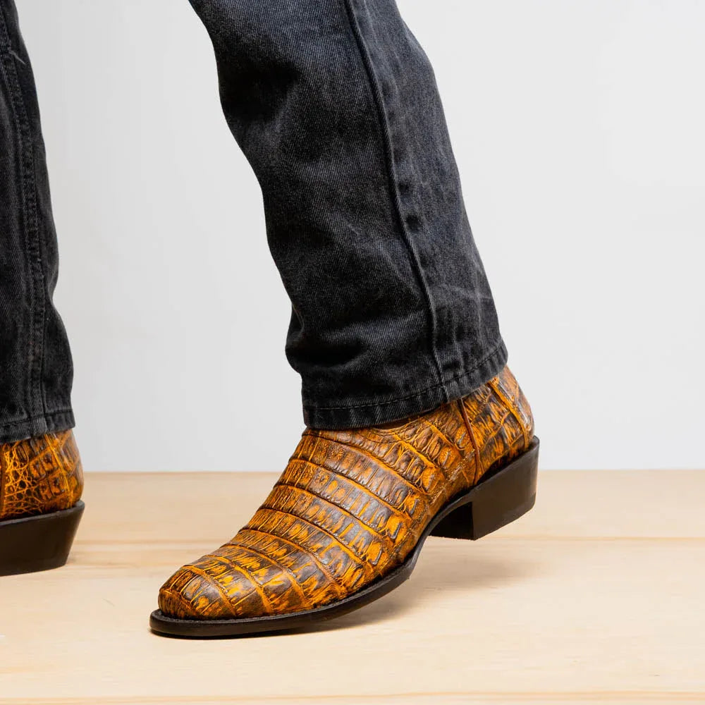 Casual outdoor scene with man wearing mustard brown caiman leather cowboy boots on gravel.
