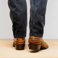 Man standing with feet crossed wearing genuine caiman belly skin cowboy boots in mustard brown.