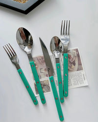 Close-up of turquoise modern French rivet cutlery with sleek handles on a kitchen table.