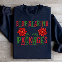 Black sweatshirt featuring the phrase 'Stop Staring At My Packages' on front with ribbed cuffs.