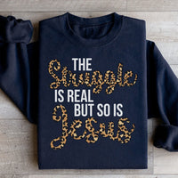 Black sweatshirt with white text reading 'The Struggle Is Real But So Is Jesus' in bold font.