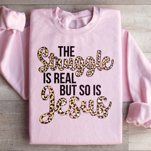 Light pink sweatshirt with large white text saying 'The Struggle Is Real But So Is Jesus'.