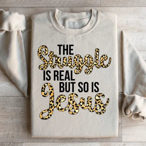 Sand-colored sweatshirt featuring bold white text stating 'The Struggle Is Real But So Is Jesus'.
