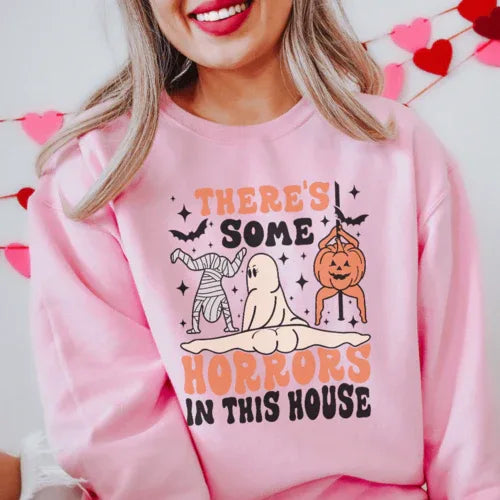 Light pink sweatshirt with bold black text 'There's Some Horrors In This House' on front.