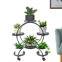 Black six-tier circular metal plant stand holding six different green potted plants in a living room corner.