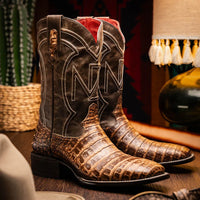 Man wearing Tucson Stone Brown cowboy boots paired with jeans standing outdoors on wooden floor.